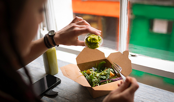 Woman pouring green sauce on a salad using paper bento box