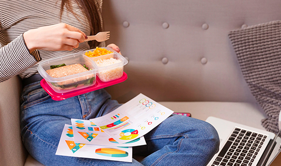 Woman working and eating using plastic lunch box on a sofa