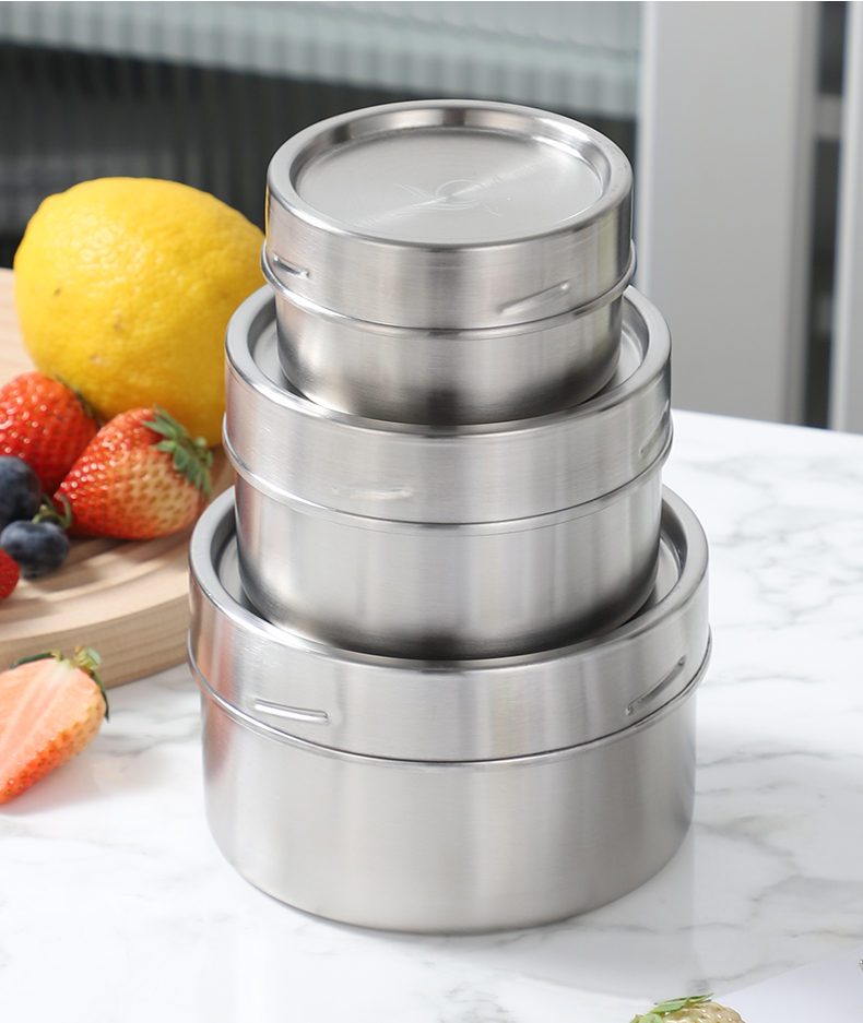 Three stacked stainless steel food storage containers with lime and berries on marble